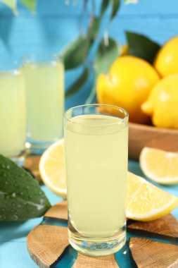 Lezzetli limoncello likörü ve limonlar açık mavi masada, yakın plan.