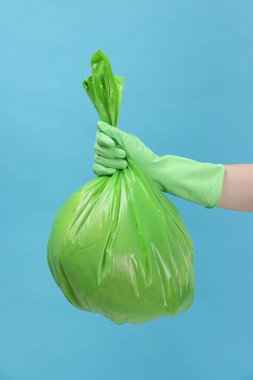 Açık mavi arka planda çöp dolu plastik poşet taşıyan kadın, yakın plan.