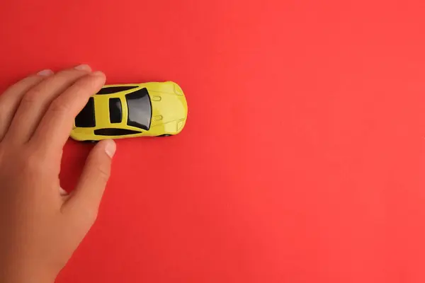 Child playing with toy car on red background, top view. Space for text