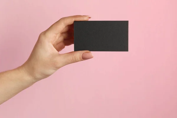 Woman with blank black business card on pink background, closeup. Mockup for design