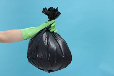 Açık mavi arka planda çöp dolu plastik poşet taşıyan bir kadın, yakın plan. Metin için boşluk