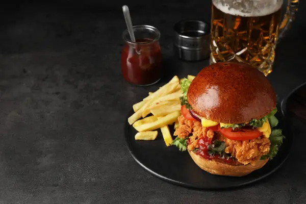 Delicious burger with crispy chicken patty, french fries, sauce and beer on black table. Space for text