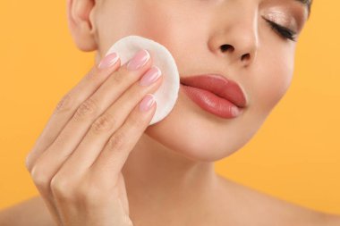 Güzel bir kadın turuncu arka planda pamuk yastıkla makyajı kaldırıyor.