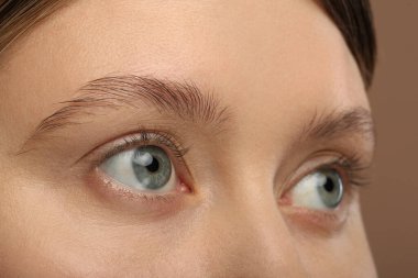 Açık kahverengi arka planda güzel doğal kirpikleri olan kadın, yakın plan.