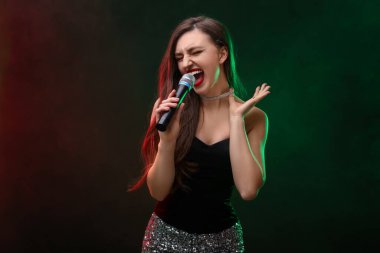 Mikrofonlu duygusal bir kadın. Arka planda renkli ışıklar eşliğinde şarkı söylüyor.
