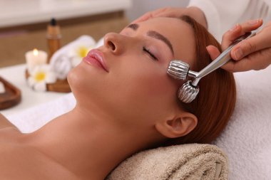 Genç bir kadın güzellik salonunda metal patenle yüz masajı yaptırıyor.