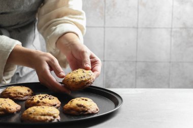 Kadın, kapalı mekândaki tepsiden lezzetli çikolatalı kurabiyeler alıyor. Metin için boşluk