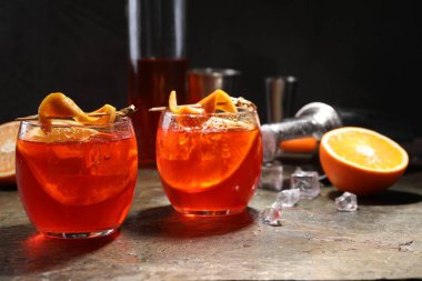 Aperol sprey kokteyli, buz küpleri ve gri desenli masada portakal dilimleri.