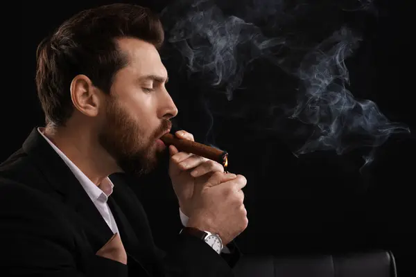 Handsome man lightning cigar on black background. Space for text