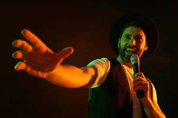 Handsome man with microphone singing in neon lights on dark background