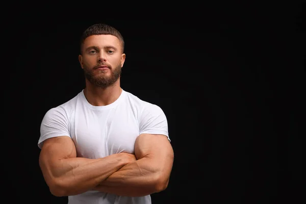 Young bodybuilder with muscular arms on black background, space for text