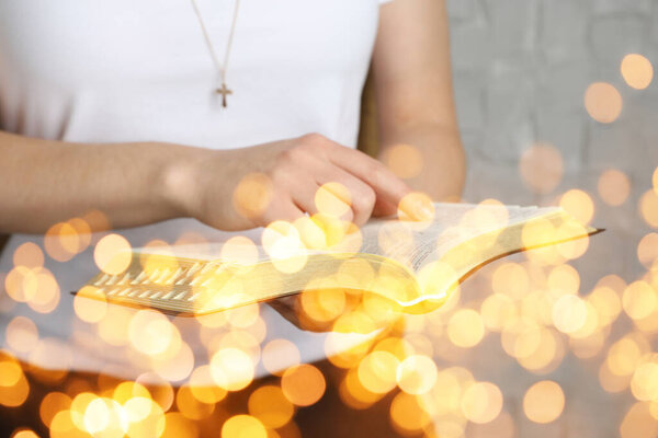 Женщина читает Библию возле белой стены, крупным планом. Эффект Боке