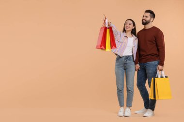 Alışveriş torbalı mutlu çift bej arka planda bir şeye bakıyor. Metin için boşluk