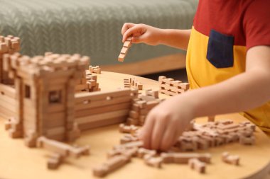 Küçük çocuk kapalı bir masada ahşap inşaatla oynuyor, yakın plan. Çocuk oyuncağı