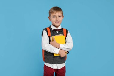 Sırt çantası ve açık mavi arka plan kitapları olan mutlu okul çocuğu.