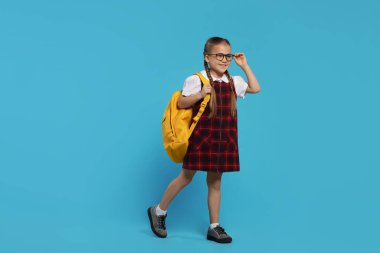 Açık mavi arka planda sırt çantalı, gözlüklü mutlu kız öğrenci.