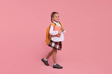 Sırt çantası ve pembe arka plan kitapları olan mutlu bir kız öğrenci.