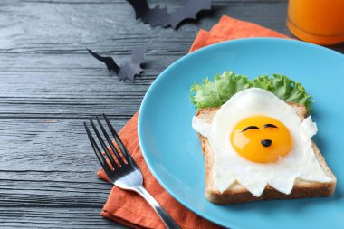 Cadılar Bayramı temalı kahvaltı siyah ahşap masada servis edilir, yakın plan. Lezzetli kızarmış ekmek ve hayalet şeklinde yumurta.