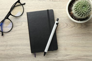 Kapalı siyah defter, kalem, bardak ve kaktüs ahşap masada, düz yatıyordu.