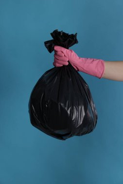 Açık mavi arka planda çöp dolu plastik poşet taşıyan kadın, yakın plan.