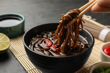 Gri masada lezzetli karabuğday çorbası (soba) yiyen bir kadın.