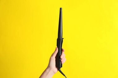 Sarı arka planda klipsiz saç maşası tutan kadın, yakın plan.