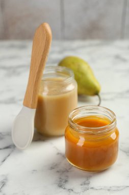 Kavanozlarda lezzetli bebek maması, beyaz mermer masada armut ve kaşık.