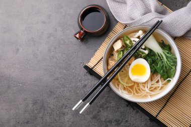 Bir kase vejetaryen ramen, soya sosu ve yemek çubukları gri masada, düz yerde. Metin için boşluk