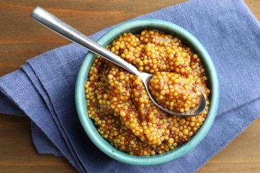 Tabakta tam tahıllı hardal ve ahşap masada kaşık, üst manzara.