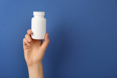 Mavi arka planda boş beyaz vitamin kavanozu tutan kadın, yakın plan. Metin için boşluk