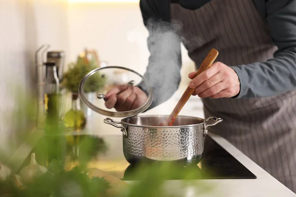 Man cooking soup on cooktop in kitchen, closeup