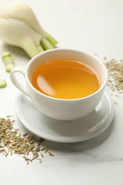 Fennel tea in cup, seeds and fresh vegetable on white marble table, closeup