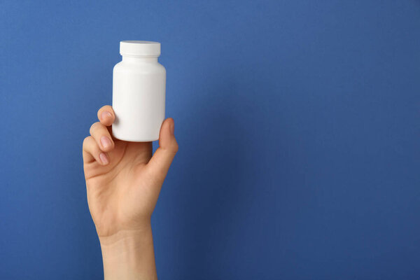 Woman holding blank white jar of vitamins on blue background, closeup. Space for text