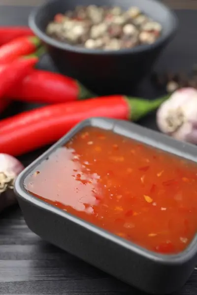Spicy chili sauce in bowl on black wooden table, closeup