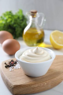 Lezzetli mayonez sosu kasede, baharatlar ve malzemeler beyaz masada, yakından.