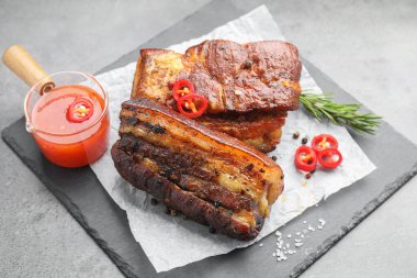 Fırında domuz göbeği, sos, biberiye ve biberiye ile servis edilmiş gri masada.