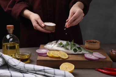 Gri masadaki çiğ dorado balığını tuzlayan kadın, yakın plan.
