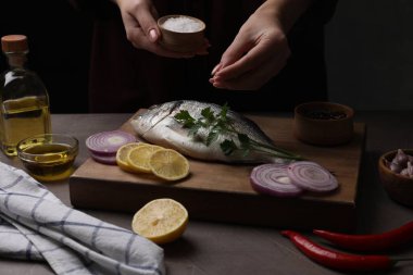 Gri masadaki çiğ dorado balığını tuzlayan kadın, yakın plan.