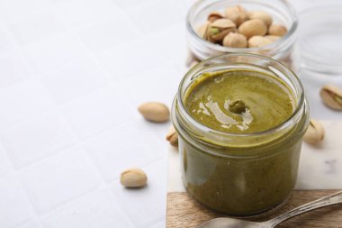 Kavanozda fıstıklı krema ve beyaz fayanslı masada fındıklar, yakın plan. Metin için boşluk