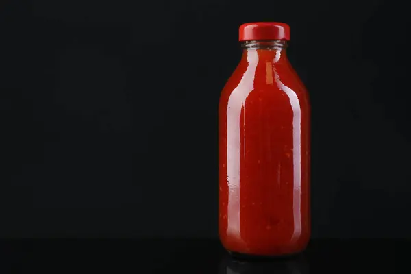 Spicy chili sauce in bottle against dark background, space for text