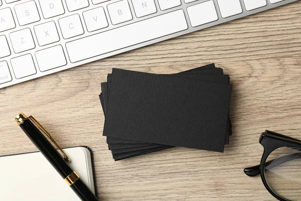 Blank black business cards, computer keyboard and stationery on wooden table, flat lay. Mockup for design