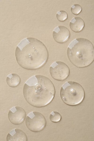 Капли косметической сыворотки на бежевом фоне, вид сверху