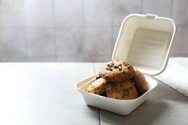 Delicious chocolate chip cookies in plastic container on light table, space for text