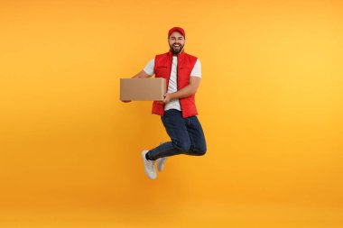 Turuncu arka planda paketle atlayan mutlu genç kurye.