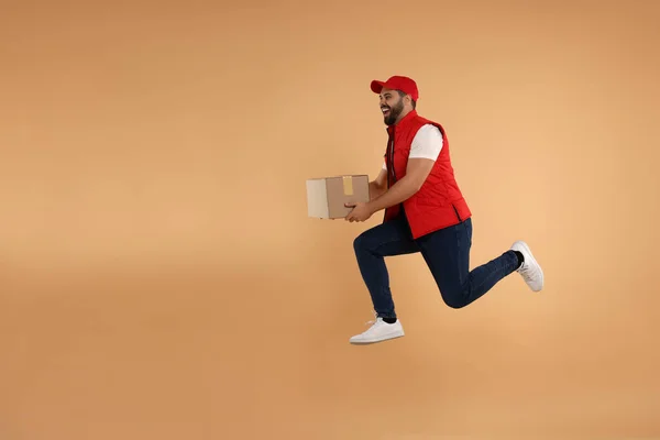 Happy courier running to deliver parcel on light brown background, space for text