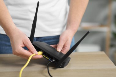 Kadın içerideki masadaki kablosuz internet yönlendiricisine ethernet kablosu yerleştiriyor.