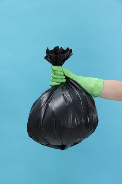 Açık mavi arka planda çöp dolu plastik poşet taşıyan kadın, yakın plan.