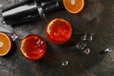 Aperol sprey kokteyli, buz küpleri ve gözlüklerdeki portakal dilimleri ve gri desenli masada sallanan salıncaklar.