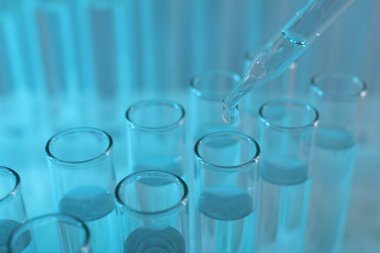 Laboratuvar analizi. Açık mavi arkaplanda pipetten cam test tüpüne sıvı damlatılıyor.