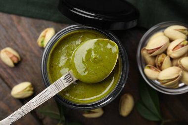 Kavanozda fıstıklı krema, ahşap masada kaşık ve fındık.